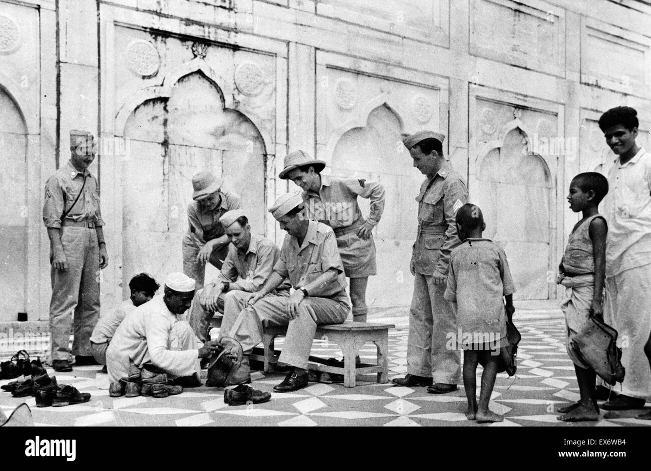 Leutnant Will R. Underwood in Indien ausgestattet mit Sandalen über seine Schuhe nach dem religiösen Brauch, als sehe mit Interesse seine Gefährten auf. 1942. Stockfoto