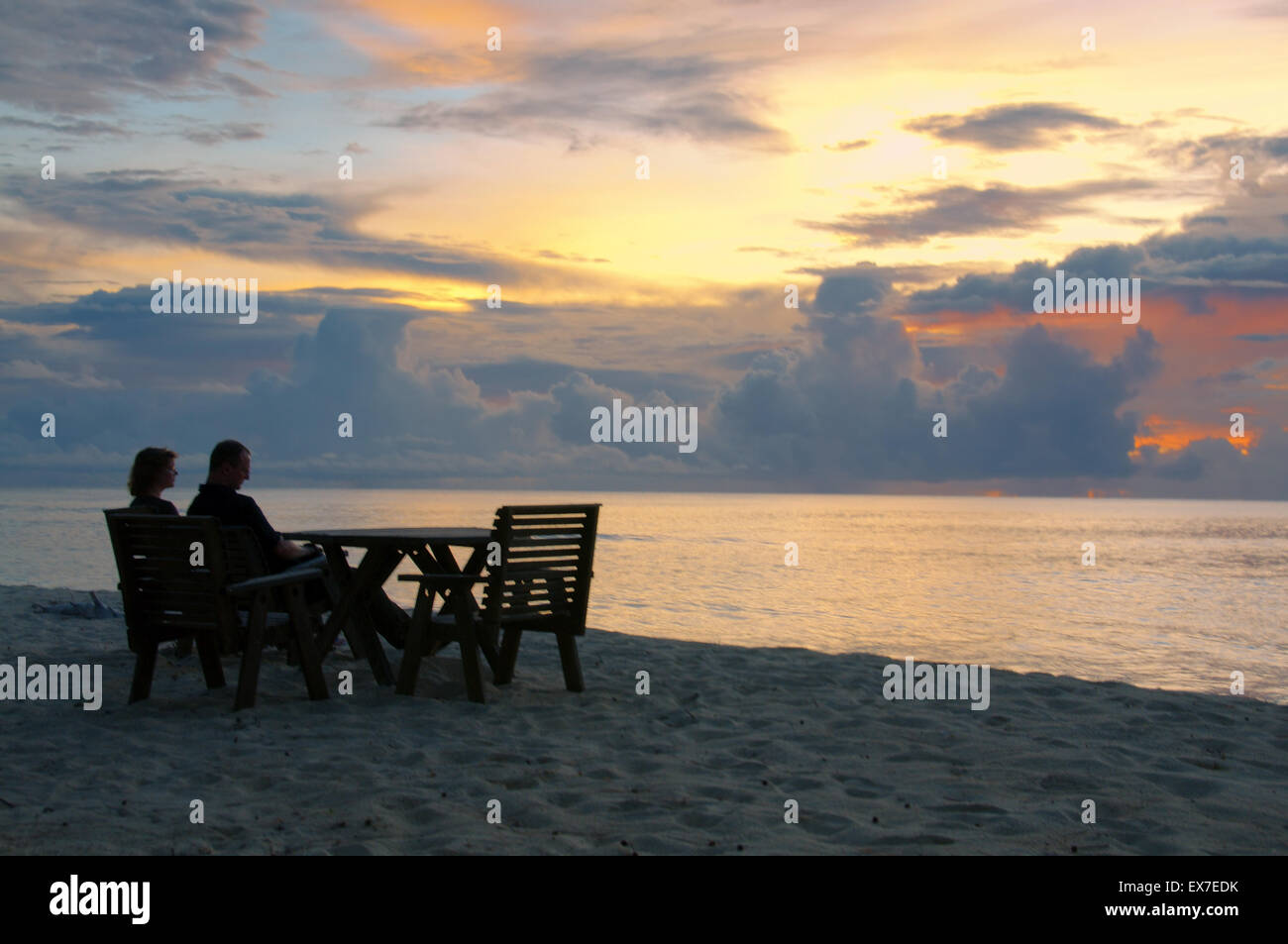 Ein Mann und eine Frau sitzen in Holzstühle an der Küste des Indischen Ozeans und bewundern Sie den Sonnenuntergang, Denis Island, Seychellen Stockfoto