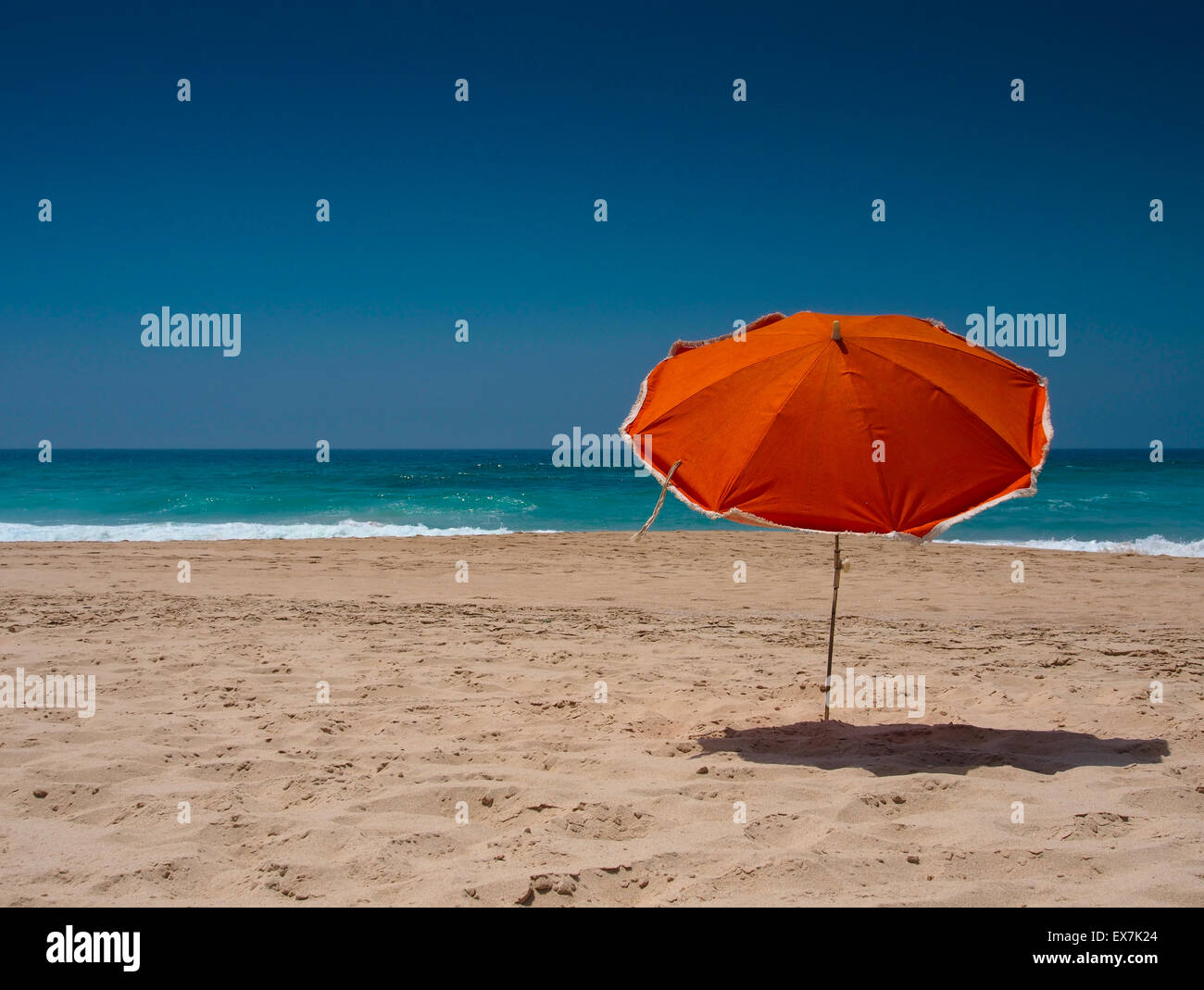 Orange Sonnenschirm am Strand mit blauem Himmel Stockfoto