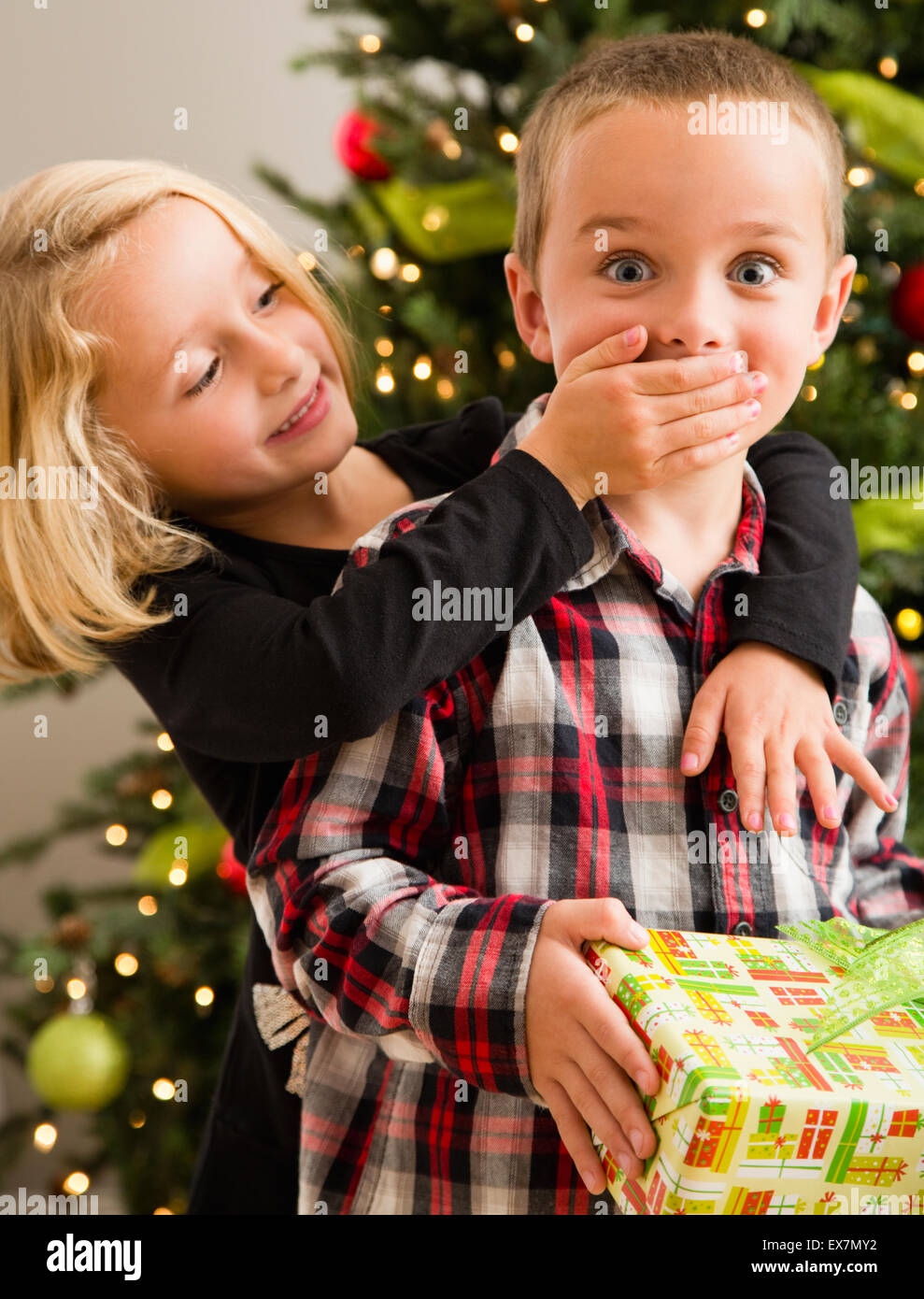 Schwester (6-7) Verkleidung Mund Bruders (6-7) mit der Hand während der Weihnachtsfeier Stockfoto