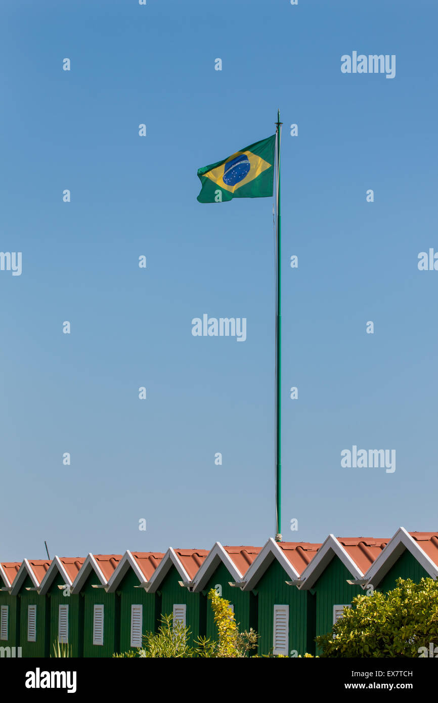 Brasilianische Flagge im Wind auf eine Fahnenstange über kleine grüne hölzerne Häuser blauen Himmel in backgruond Stockfoto