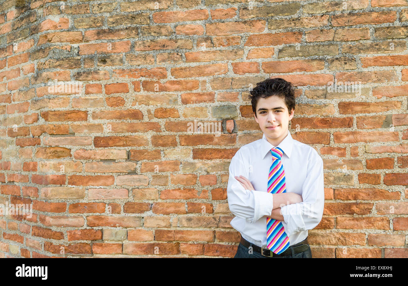 Hübscher kaukasischen junge trägt ein weißes Hemd und eine regimental Krawatte mit rot, Fuchsia, orange, blau, indigo und weißen Streifen ist seine Arme vor einer Mauer bei Sonnenuntergang überqueren. Stockfoto