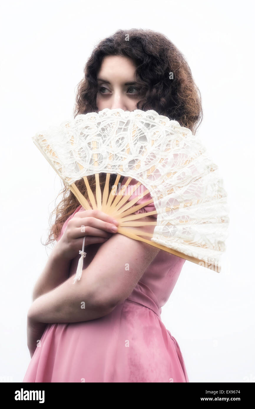 eine schöne Frau mit langen lockigen Haaren in einem rosa Kleid mit einem weißen Lüfter Stockfoto