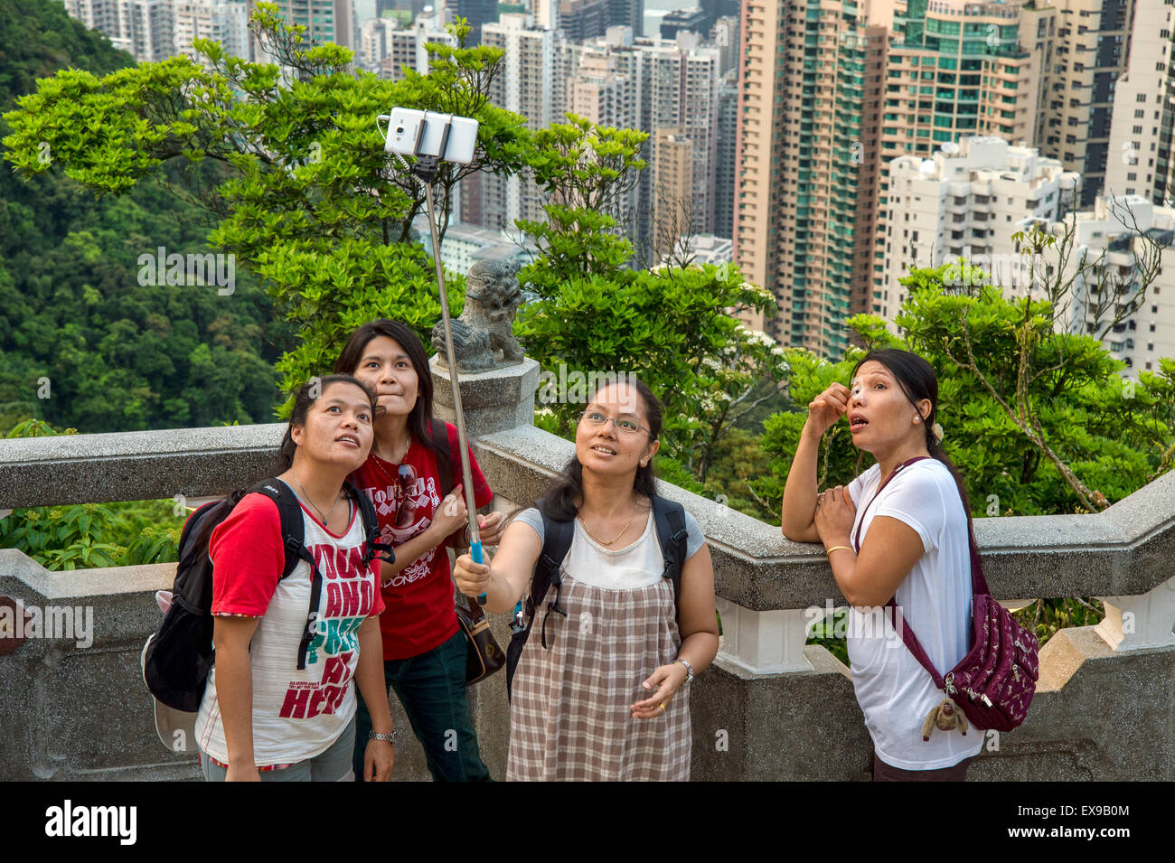 drei asiatische Mädchen mit einem Selfie stick vor Hong Kong Skyline von Victoria peak Stockfoto