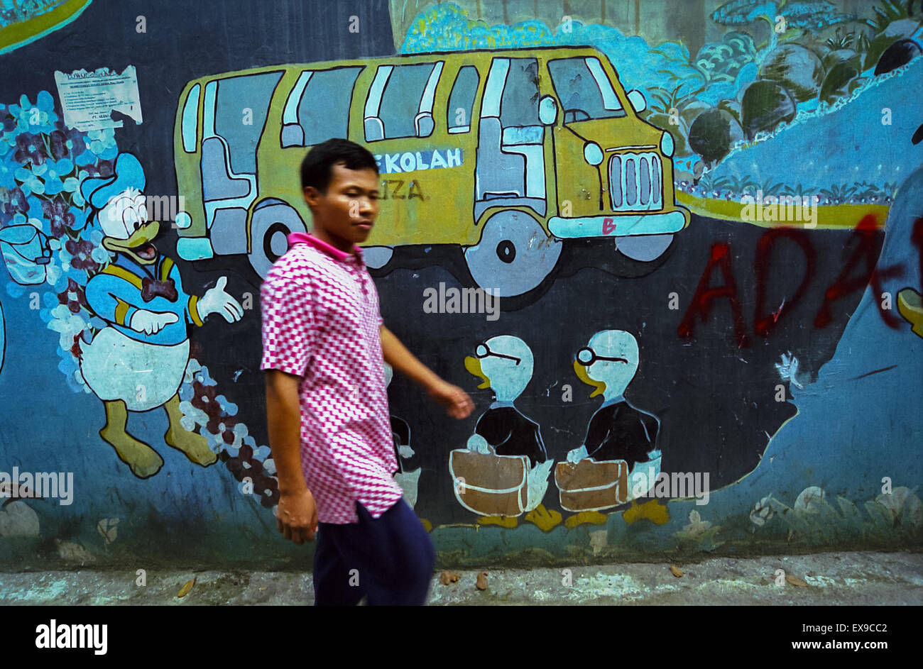 Ein Fußgänger zu Fuß auf einer Gasse mit Comic-Figuren Wandgemälde in Palmerah Bereich, Jakarta, Indonesien. Stockfoto