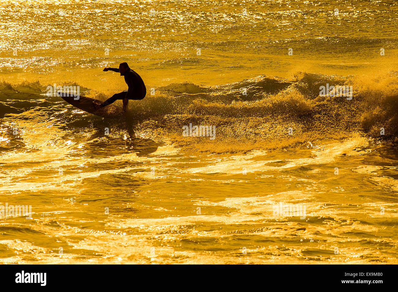 Ein Surfer am Fistral als die Sonne untergeht. Stockfoto
