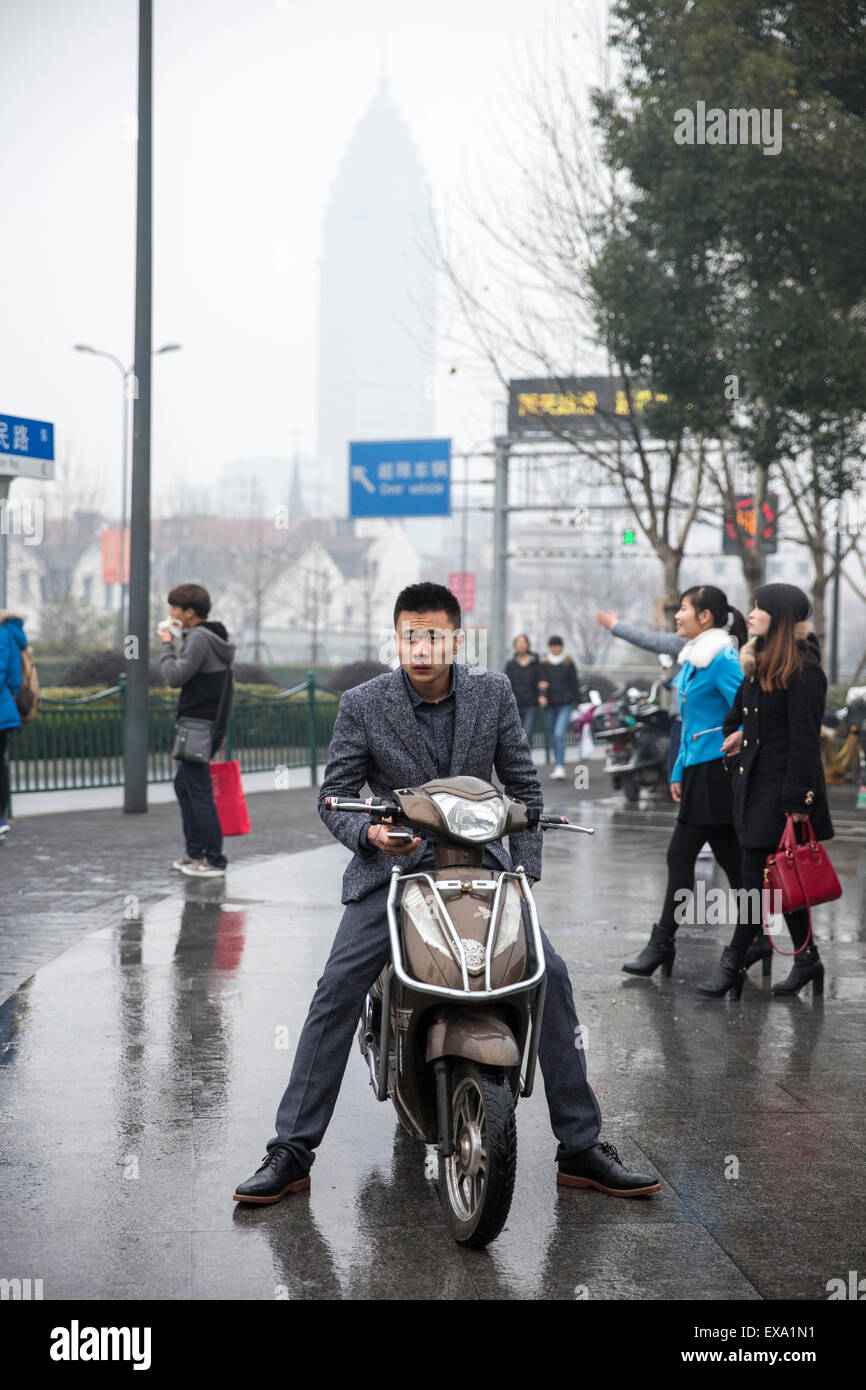 China, Shanghai, junger Mann trägt Anzug während während des Wartens auf Motorroller auf Straße Zebrastreifen auf regenreichen Winter-Nachmittag Stockfoto