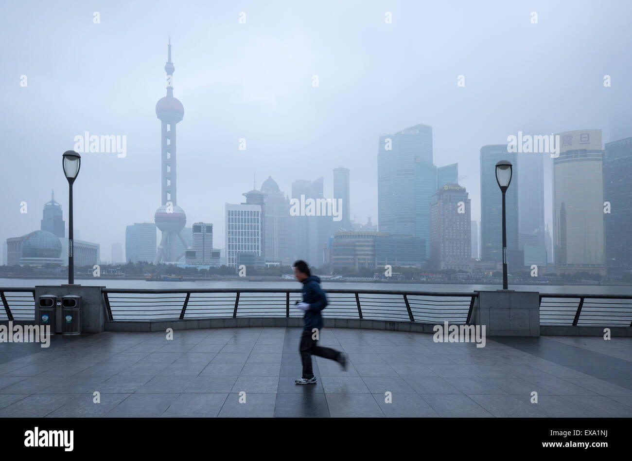 China, Shanghai, Jogger führt vorbei an Skyline von Pudong District in niedrigen Wolken Huangpu Fluss entlang an Wintermorgen verloren Stockfoto