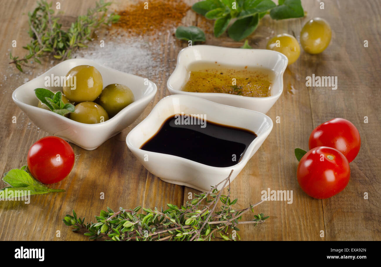 Dressing Zutaten auf einem hölzernen Hintergrund. Olivenöl, Balsamico-Essig, Kräuter, Salz und Pfeffer. Selektiven Fokus Stockfoto