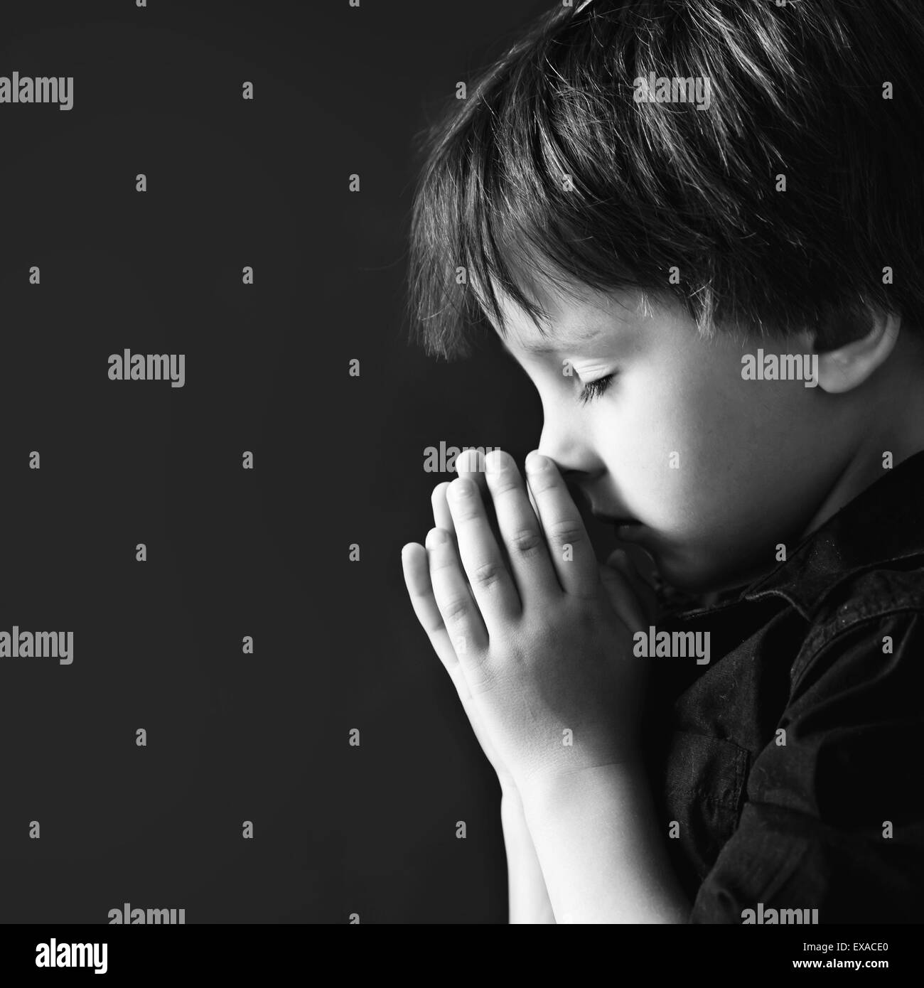 Kleiner Junge, beten, beten, Kind isoliert schwarzen Hintergrund Stockfoto