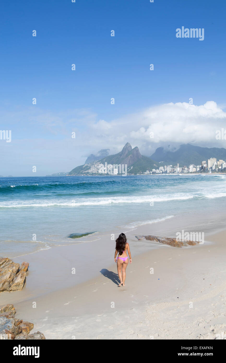 Eine 20-25 jährige Junge brasilianische Frau am Strand von Ipanema mit den Morro Dois Irmãos Hügeln in der Ferne, Rio De Janeiro, Brasilien Stockfoto