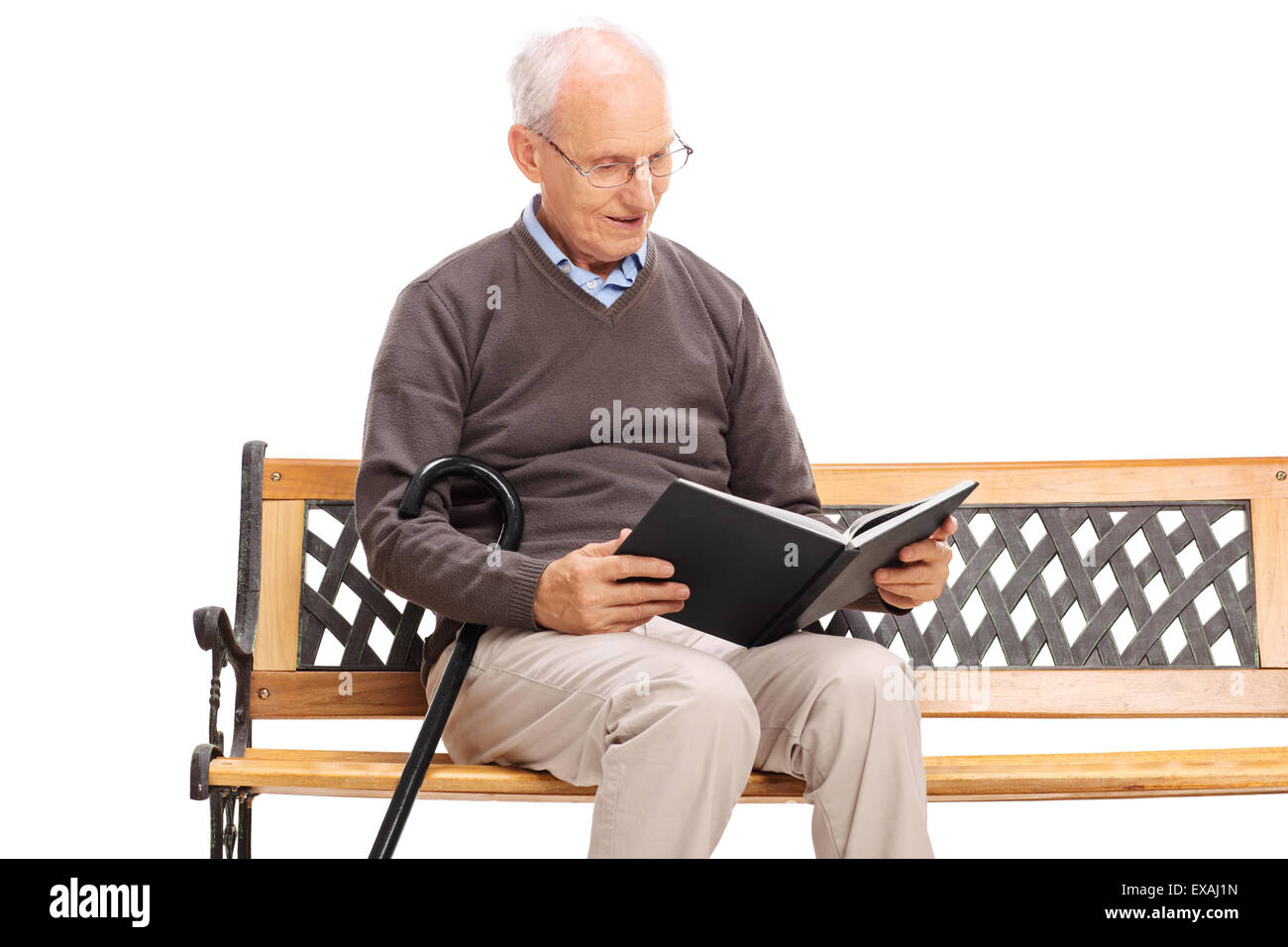 Freudige Senior Lesen eines Buches sitzt auf einer Holzbank und hält einen Stock isoliert auf weißem Hintergrund Stockfoto