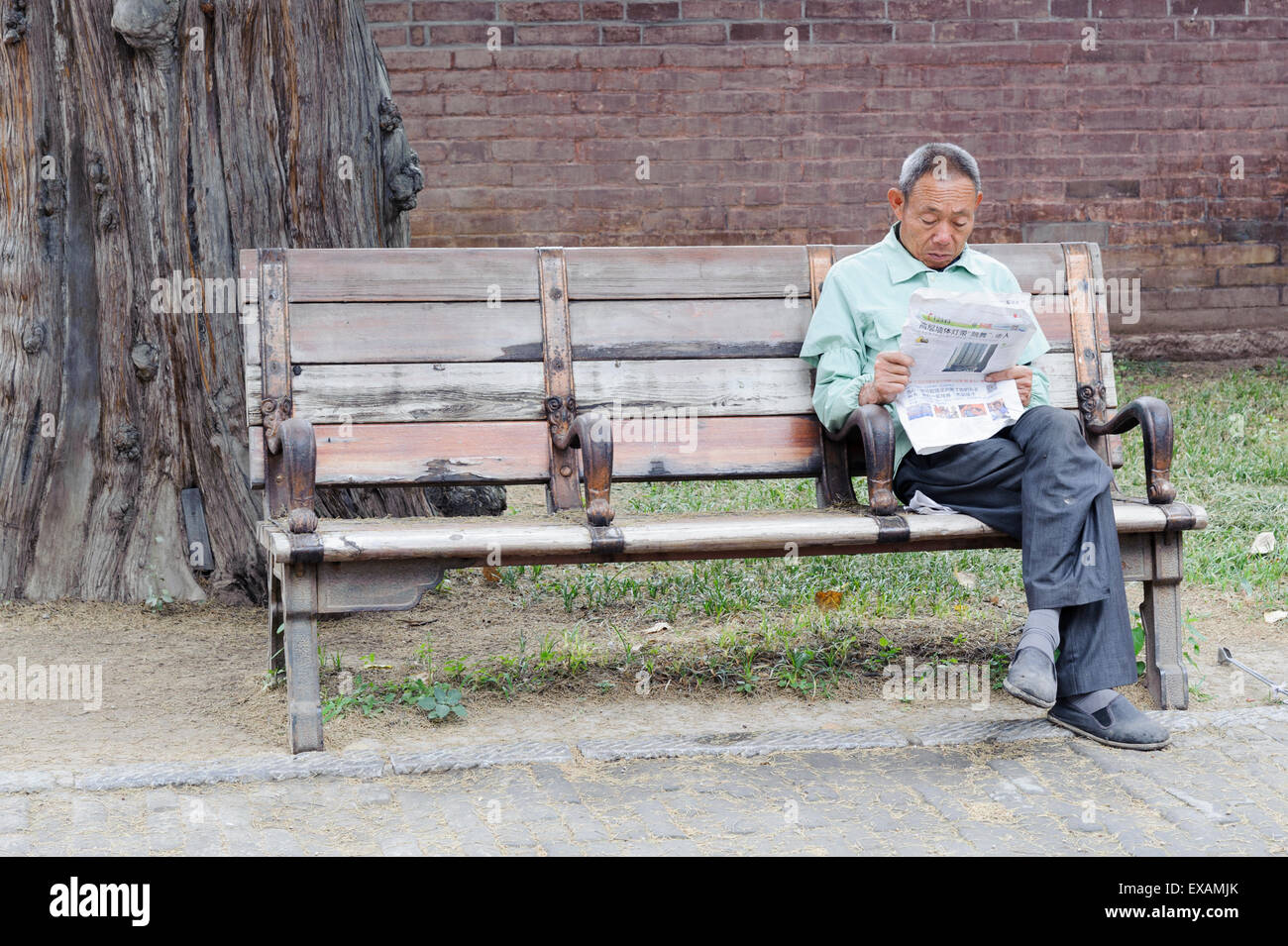 Garten-Arbeiter Zeitungslektüre am Eingang zu Konfuzius Wald und Grabstätte. Er ist auf eine alte Bank sitzen. Stockfoto