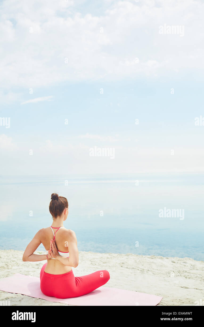 Junge Frau mit gekreuzten Beinen und Arme hinter Rücken sitzen auf Sand vom Wasser Stockfoto