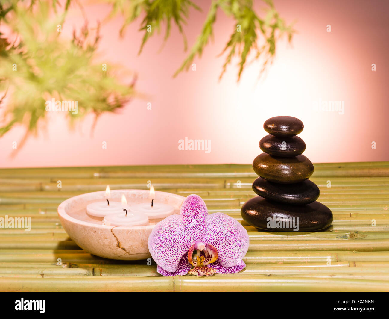 Stillleben mit Stapel von Steinen auf Bambus, Orchidee und Kerzen warme Atmosphäre Stockfoto