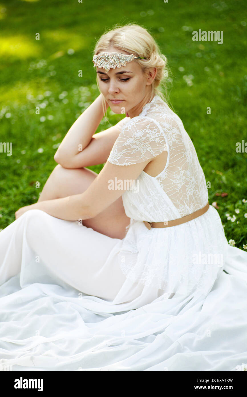 Frau sitzt in dem weißen Kleid auf Wiese Stockfoto