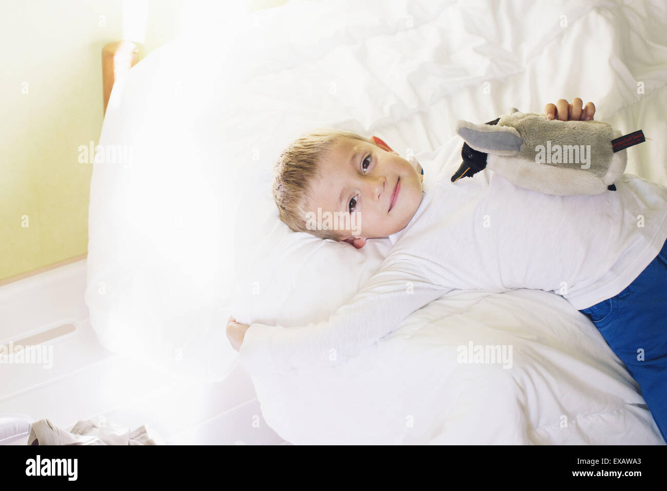 Junge auf Bett liegend mit ausgestopften Pinguin Stockfoto