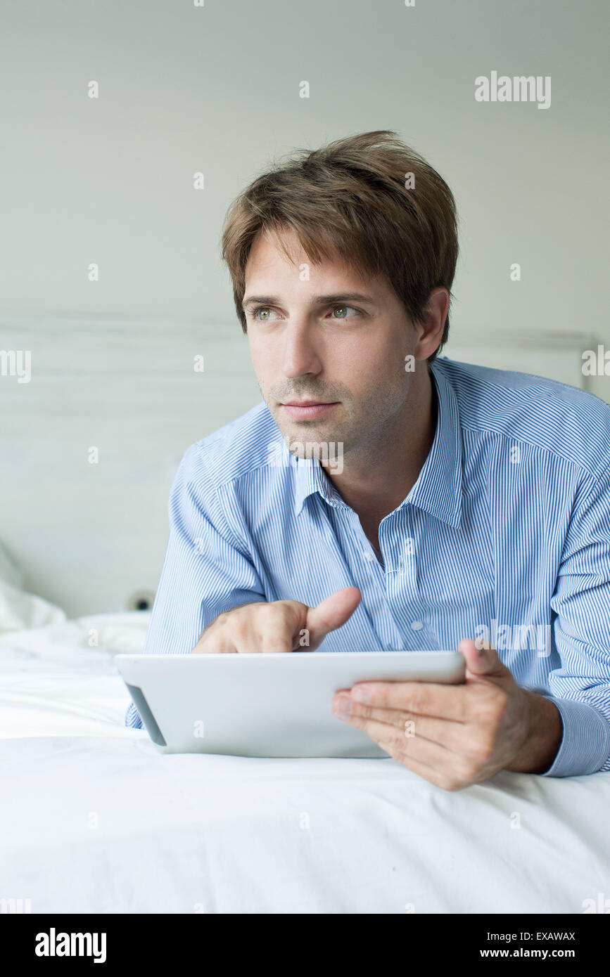 Mann im Bett mit digital-Tablette, wegschauen mit kontemplativen Blick Stockfoto