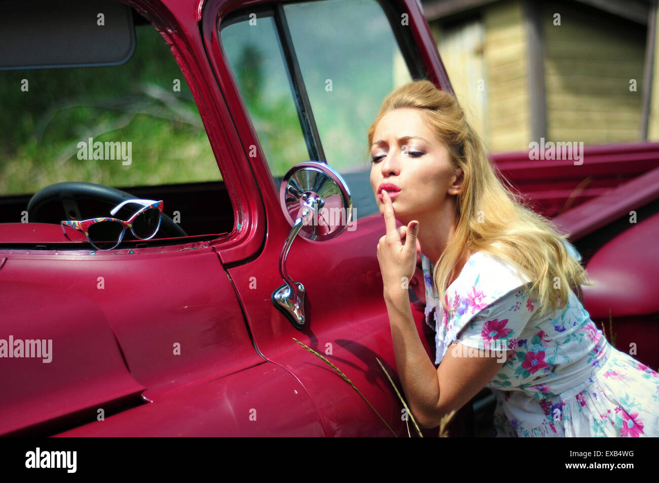 Junge Frau in ein Vintage-Kleid Blick in den Spiegel ein Retro-rotes Auto Stockfoto
