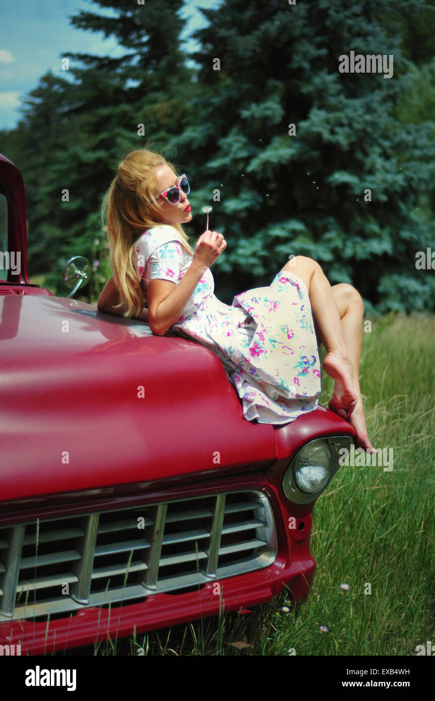 Junge Frau-Vintage-Stil, sitzt auf einem Retro-rotes Auto mit einem Löwenzahn Stockfoto