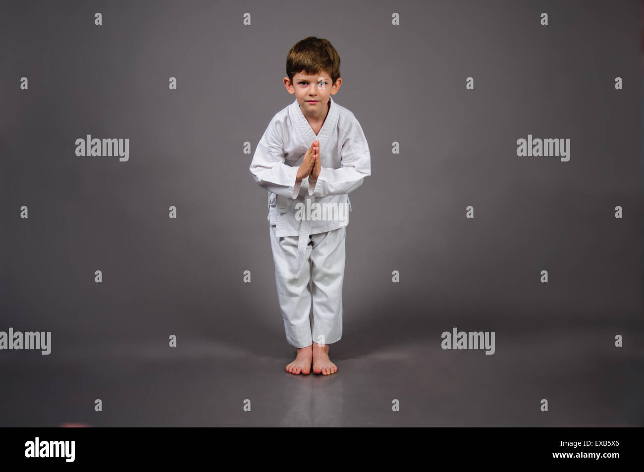 Karate-junge in Verbeugung stellen tragen weiße Kimono auf grauem Hintergrund Stockfoto