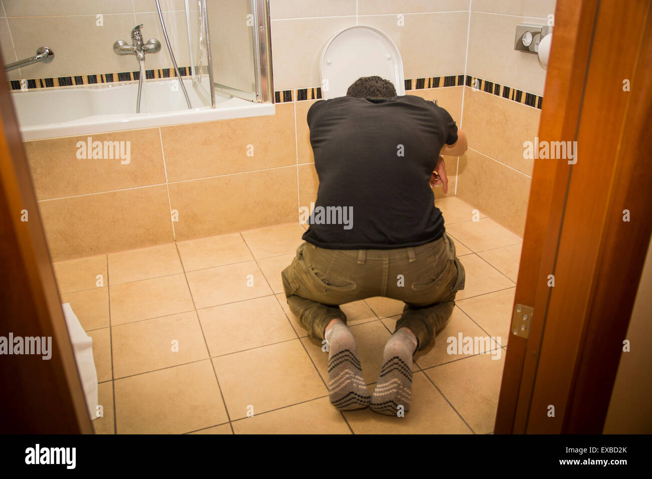 Rückansicht eines betrunkenen jungen Mannes Erbrechen in der Toilette zu Hause während in kniende Position. Stockfoto