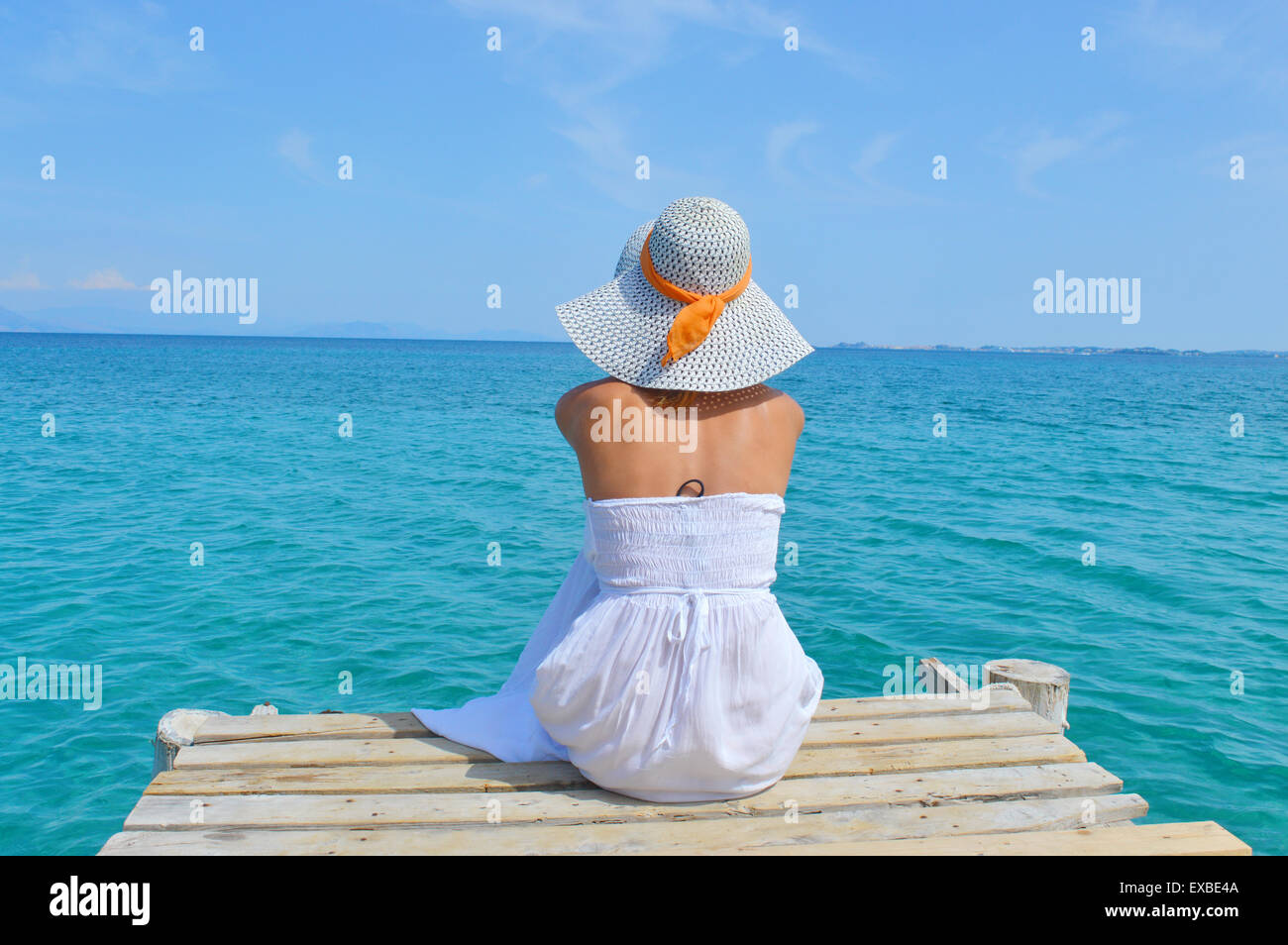 Junge Frau in einem weißen Kleid mit Blick auf das Meer aus einem dock Stockfoto