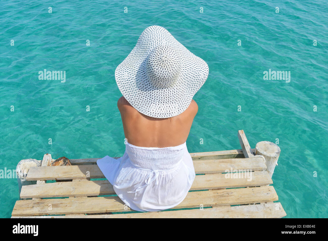 Junge Frau in einem weißen Kleid mit Blick auf das Meer aus einem dock Stockfoto
