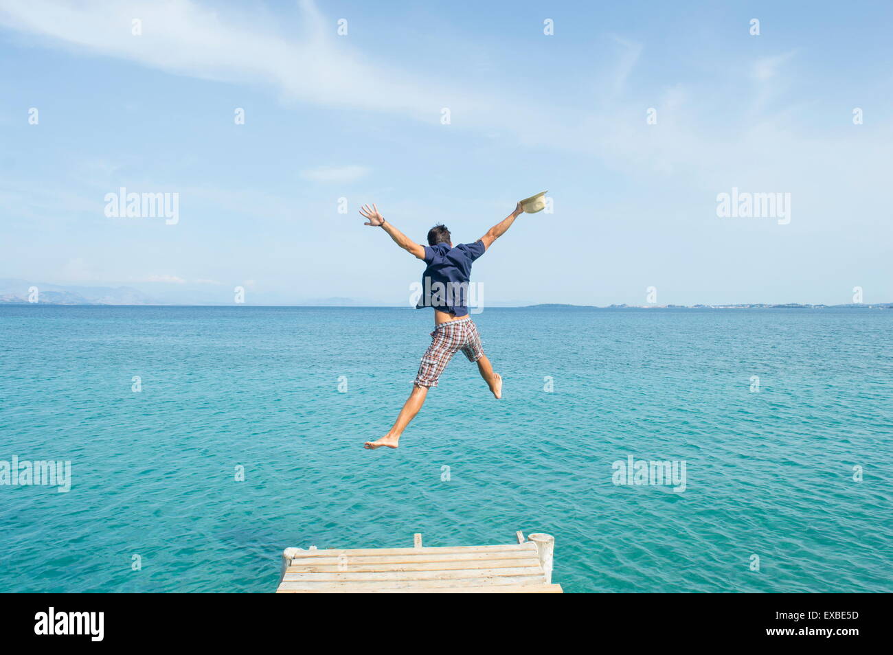 Junger Mann springt aus dem Dock in das Meer mit seinen Kleidern auf Stockfoto