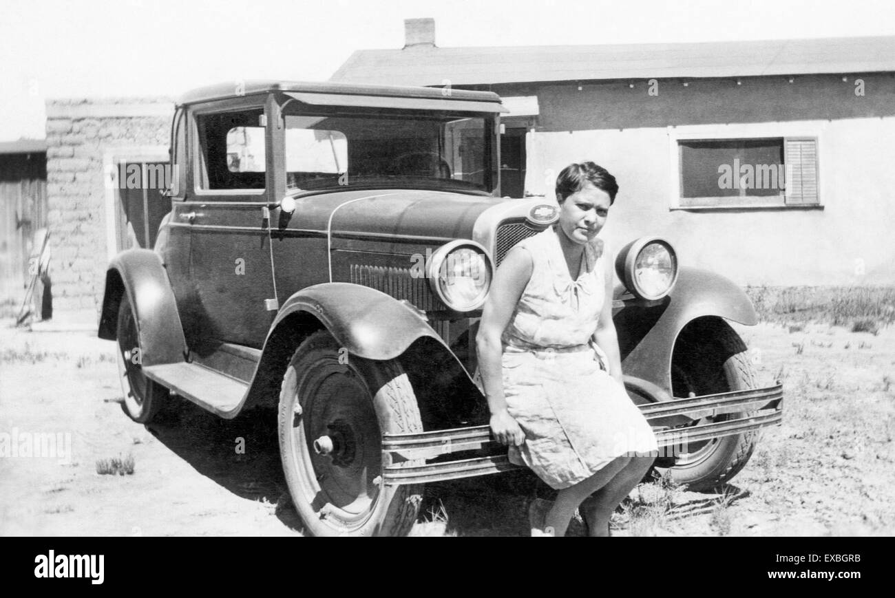 Eine Frau sitzt vor einem Adobe-Haus in Belen, New Mexico, auf der Stoßstange ihres Chevrolet Autos im Jahr 1929. Stockfoto