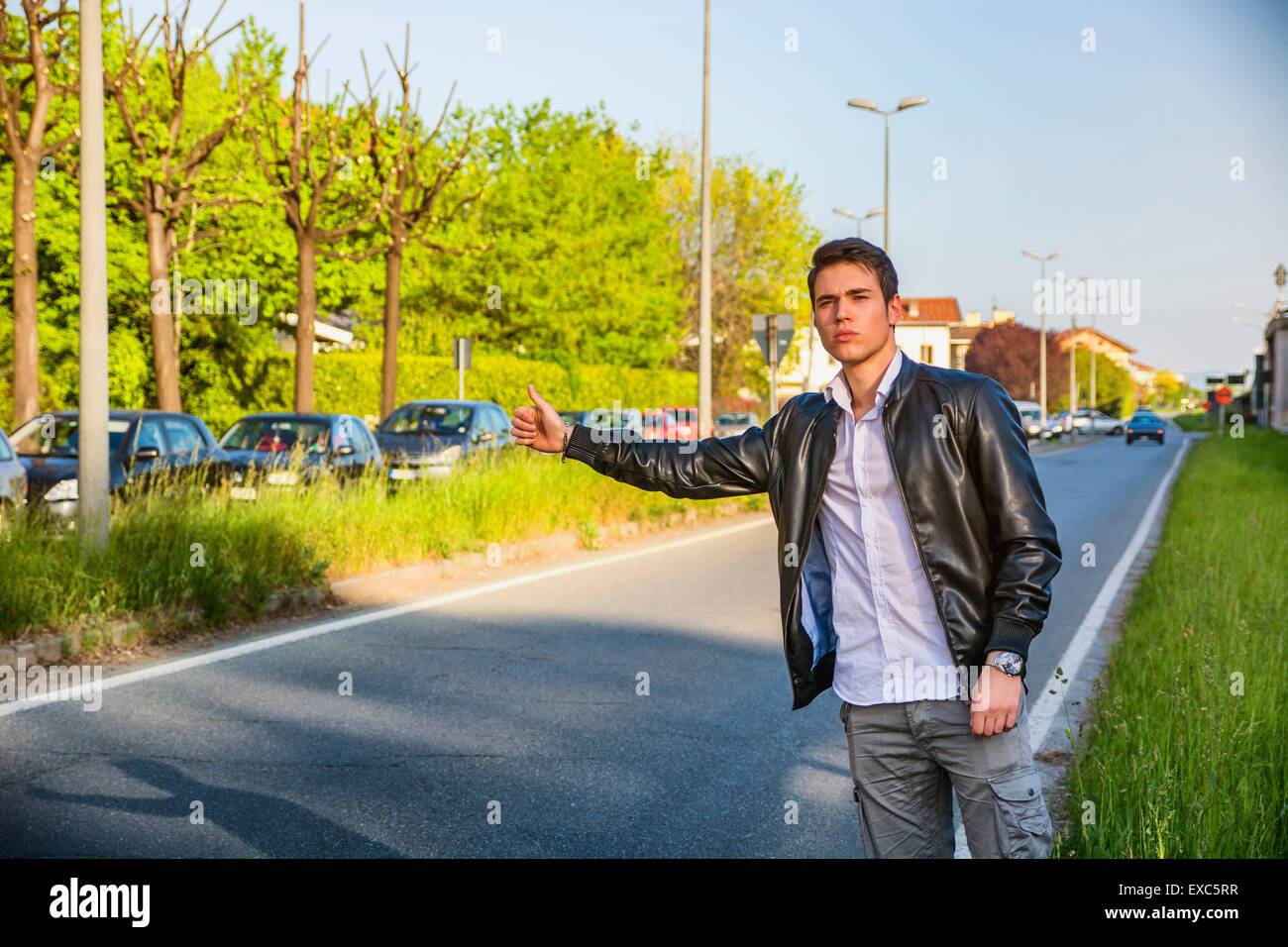 Hübscher junger Mann, ein Tramper warten Auto am Straßenrand in der Stadt, tragen schwarze Lederjacke Stockfoto