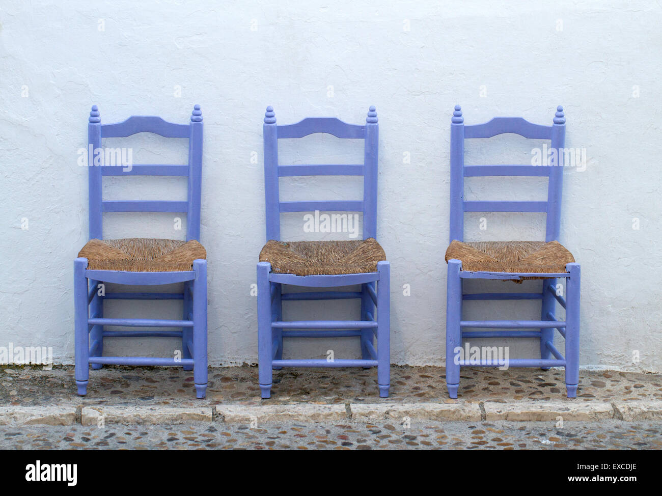 Alte blaue Holzstühle allein auf der mediterranen Straße auf einer weißen Wand Stockfoto