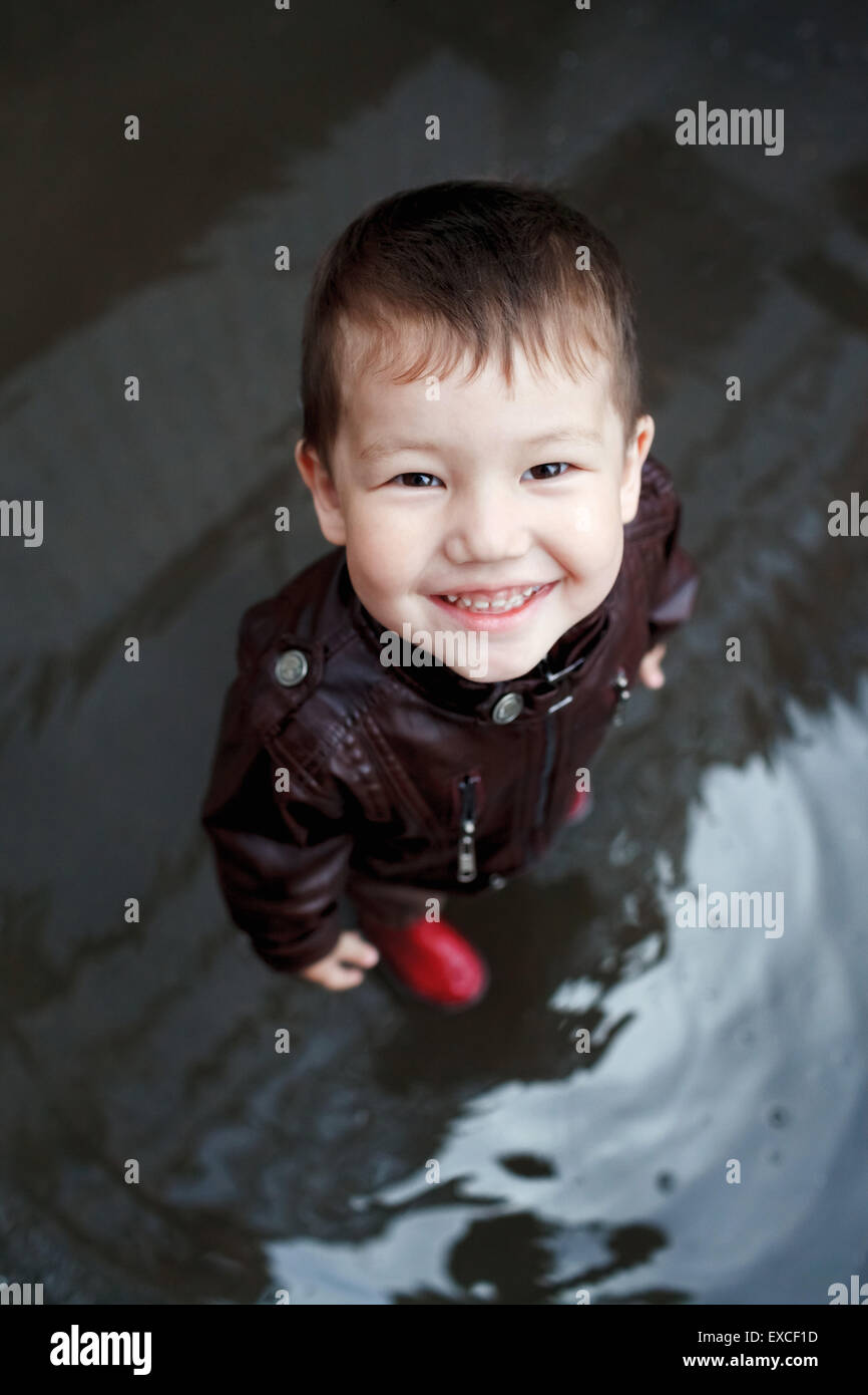 Junge in Gummistiefeln spielt in einer Pfütze. Stockfoto