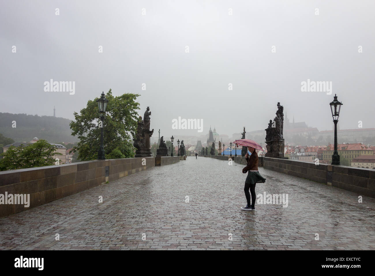 Karlsbrücke, Praque, Tschechische Republik: Junge Frau, die zu Fuß über die Brücke auf einem nassen und windigen Morgen, bevor die Massen ankommen Stockfoto