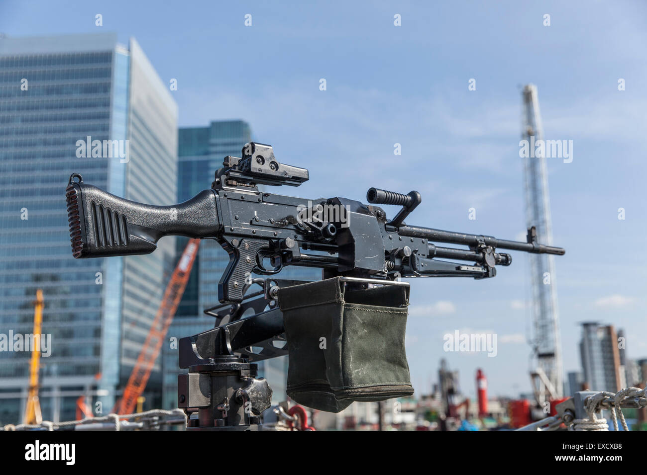 Allzweck-Maschinengewehr im Fokus auf dem Deck eines Schiffes mit Schwerpunkt moderne Gebäude und Kräne in London unscharf Stockfoto