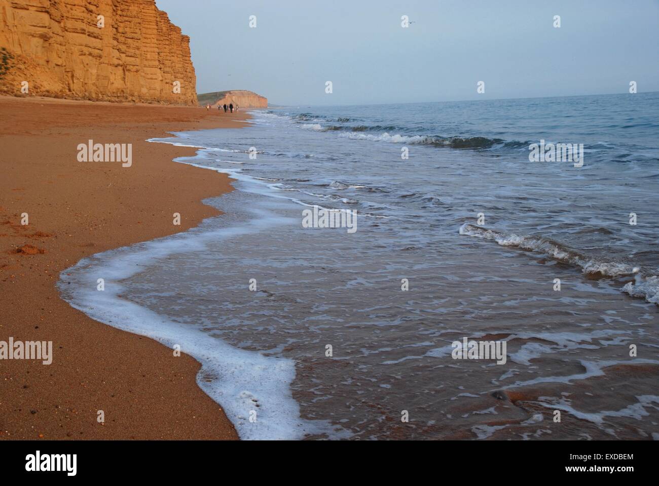 Wellen, die sanft den Strand unter den Sandsteinklippen von West Bay, Dorset, Großbritannien, umschlagen Stockfoto
