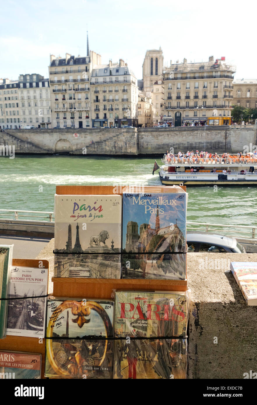 Bücher bei Bouquinistes entlang der Seine mit einem vorbeifahrenden Touristen Kahn, Boot, Paris, Ile De La Cité, Frankreich. Stockfoto