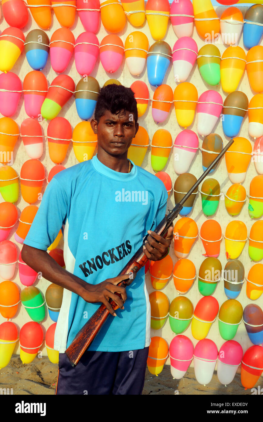 Junge indische Mann hält Luftgewehr am Strand Spaß stall mit Ballon-Ziele Stockfoto