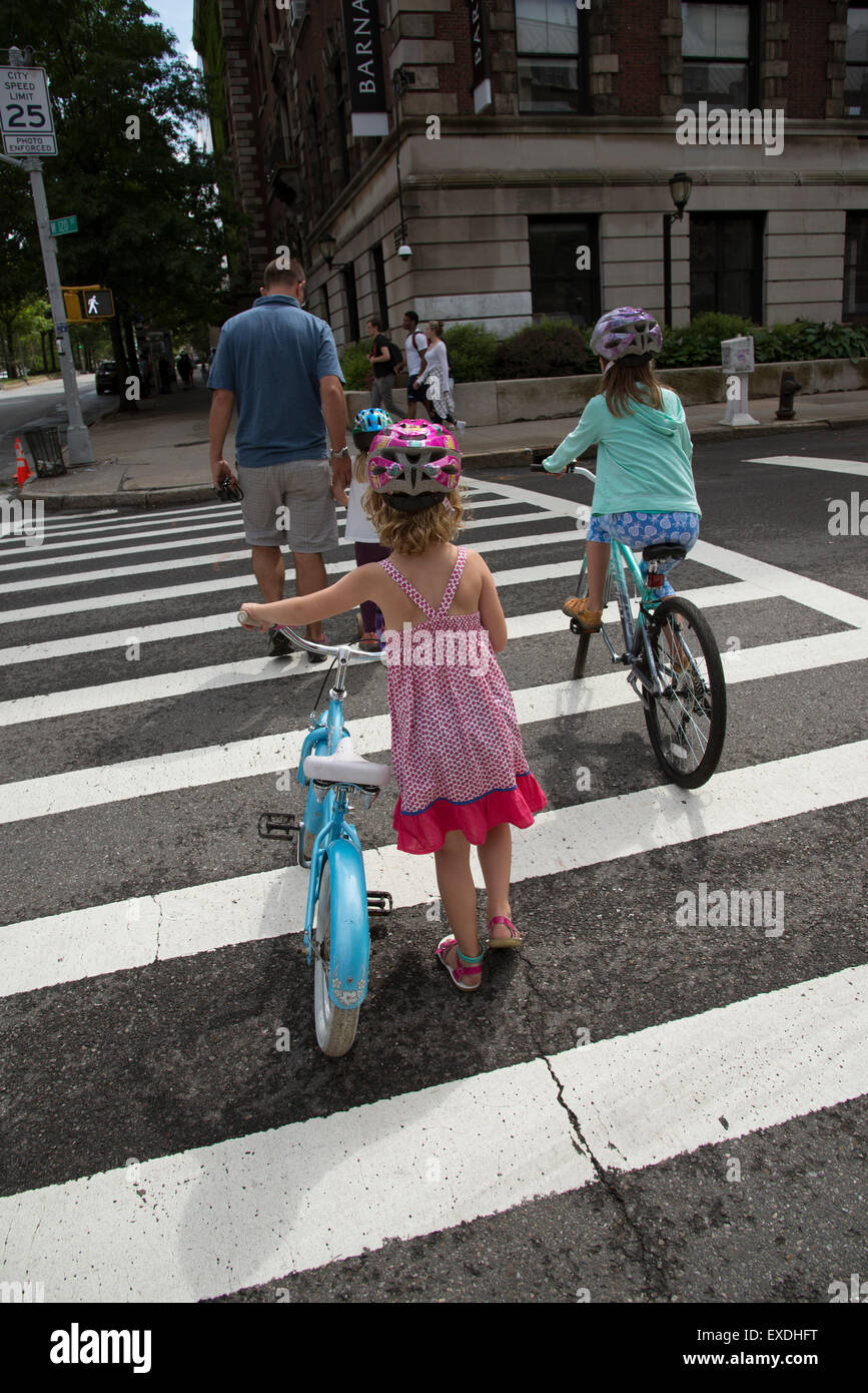 Kleinen Kindern auf dem Fahrrad über die Straße mit einem Erwachsenen A Rückansicht New York USA Stockfoto
