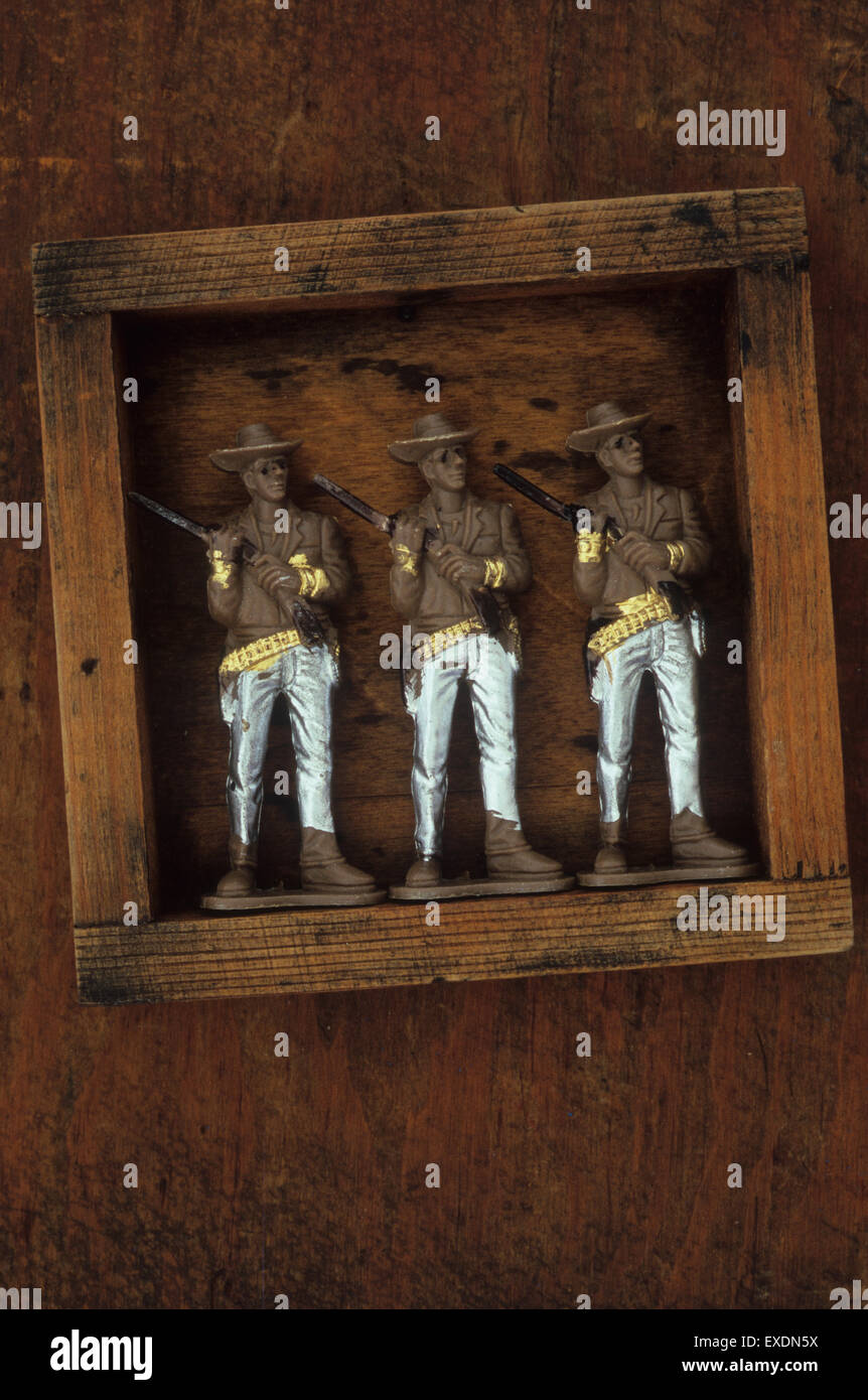 Drei identische Kunststoffmodellen Cowboys mit silbernen Hose halten Gewehre über Schultern stehend in Holzkiste Stockfoto