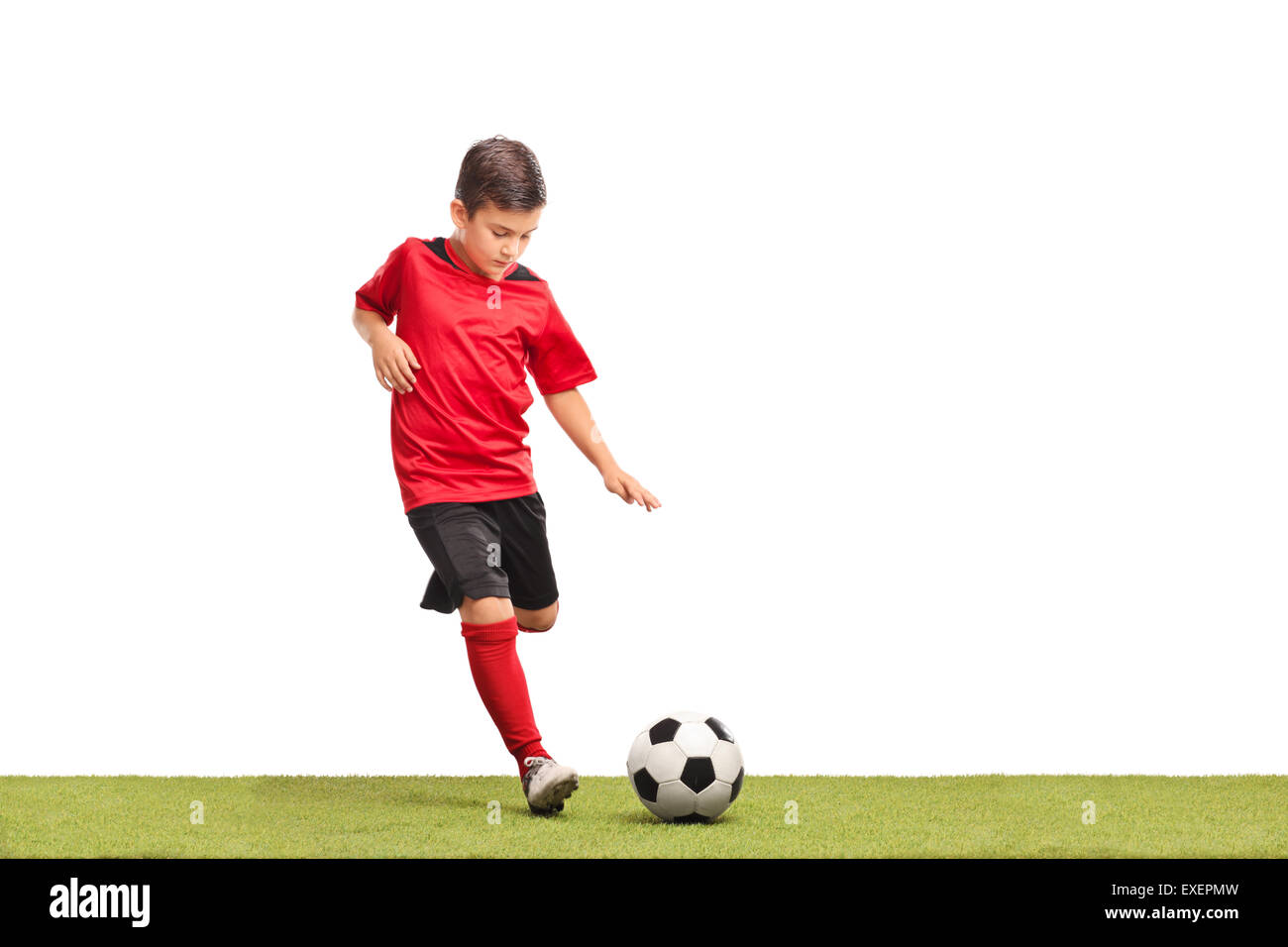 Kleines Kind im roten Fußballtrikot treten einen Fußball auf einer Rasenfläche, die isoliert auf weißem Hintergrund Stockfoto
