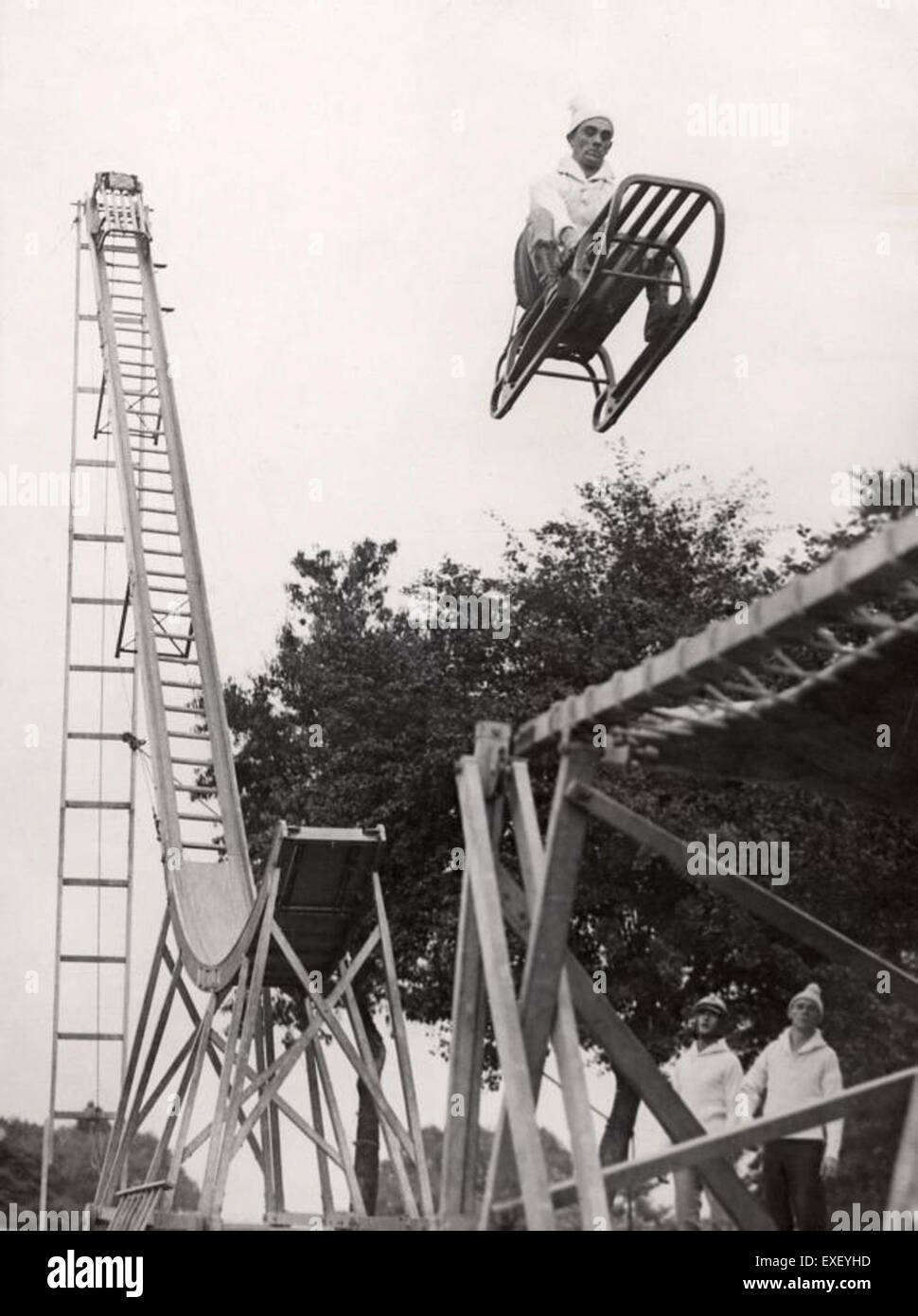 Dieses Vintage-Foto zeigt einen Schlitten, der von einer Schanze startet und einen Einblick in eine vergangene Ära des Wintersports bietet. Die Szene ist sowohl energiegeladen als auch historisch und spiegelt die frühe Entwicklung der Winterathletik wider. Stockfoto