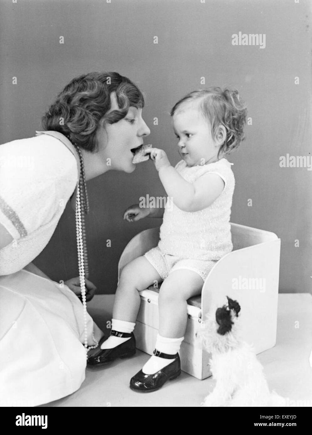 Ein zarter Moment, in dem ein Baby seiner Mutter einen Keks füttert, symbolisch für die Bindung zwischen Eltern und Kind und widerspiegelt die fürsorgliche Natur familiärer Beziehungen. Stockfoto