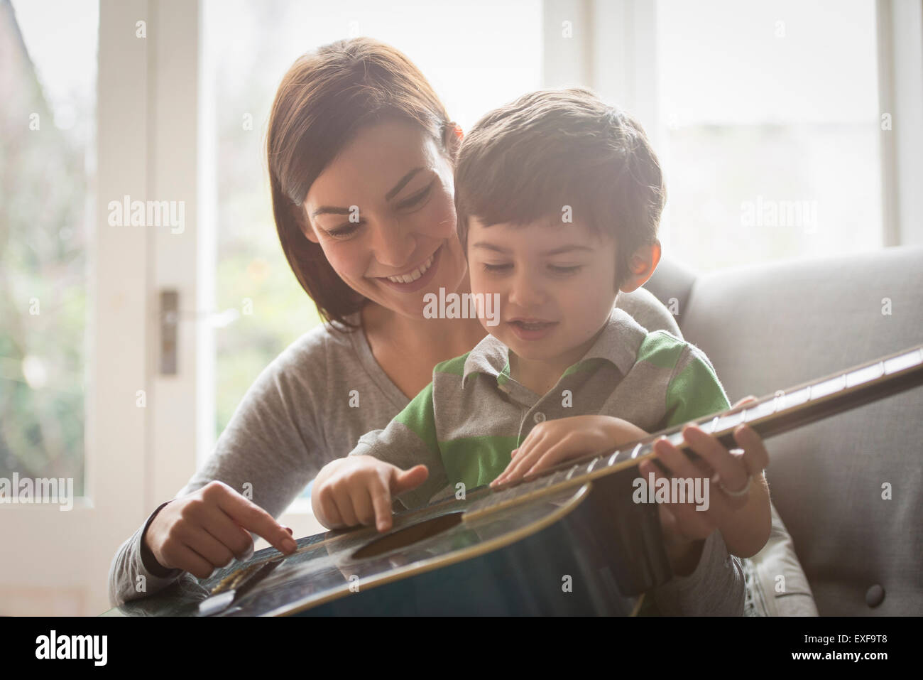 Junge auf Mutters Schoß sitzen und lernen, Gitarre zu spielen Stockfoto