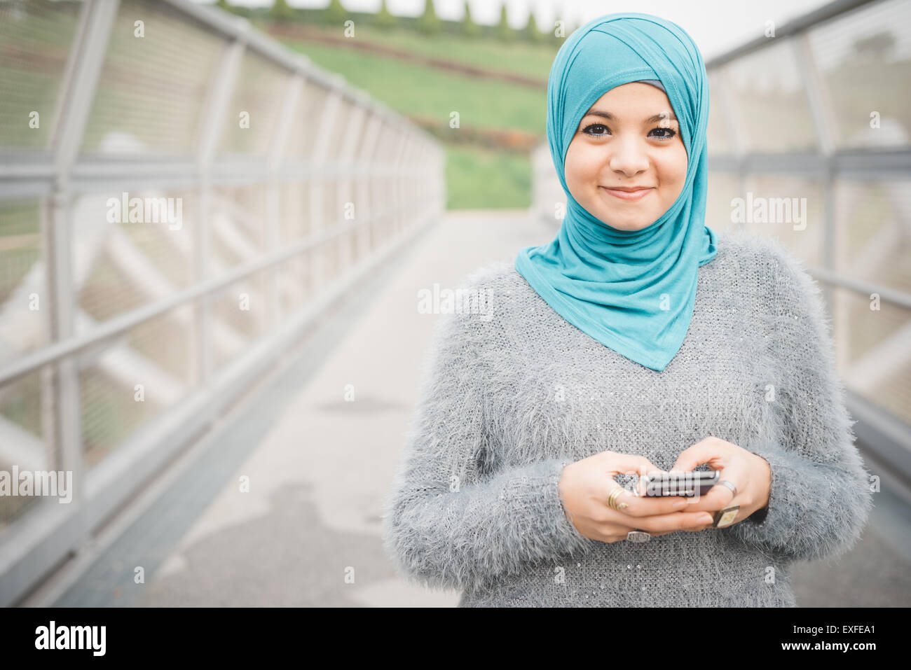 Porträt der jungen Frau mit türkisfarbenen Hijab mit Smartphone auf Steg Stockfoto