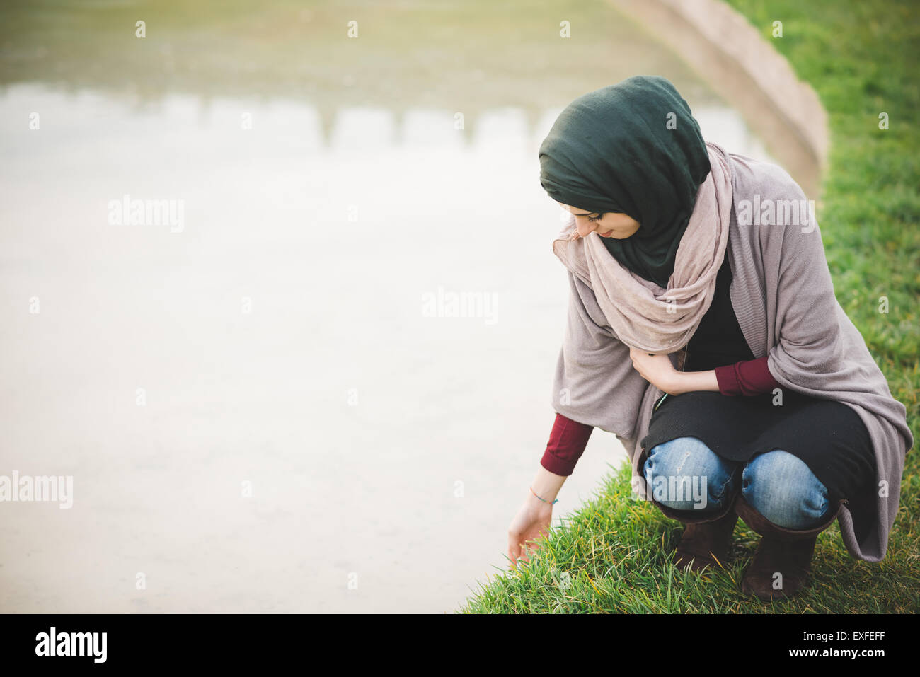 Junge Frau trägt Hijab hocken neben dem Park-See Stockfoto