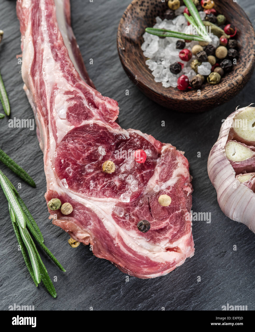 Rohe Lammkoteletts mit Knoblauch und Kräutern auf dem alten Holztisch. Stockfoto