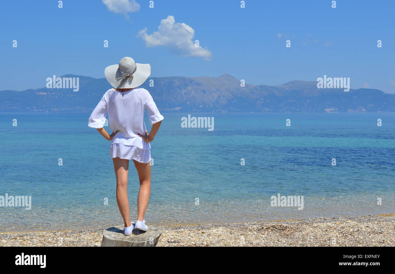 Junge Frau, Blick auf die Berge über dem Meer stehen auf dem Baumstamm Stockfoto
