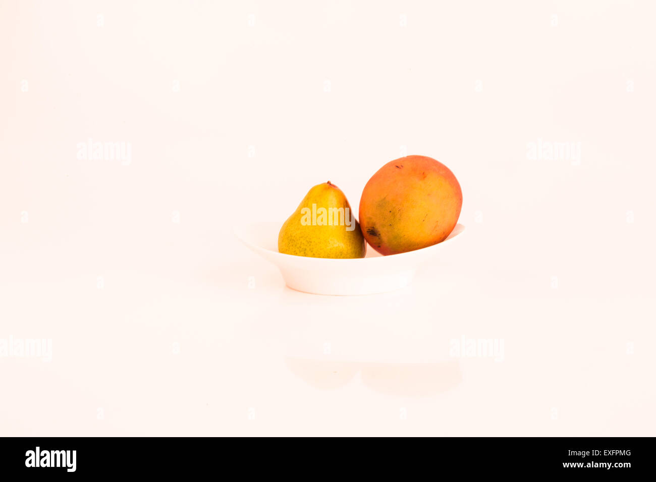 Eine Birne neben einer Mango auf einem weißen Teller Stockfoto