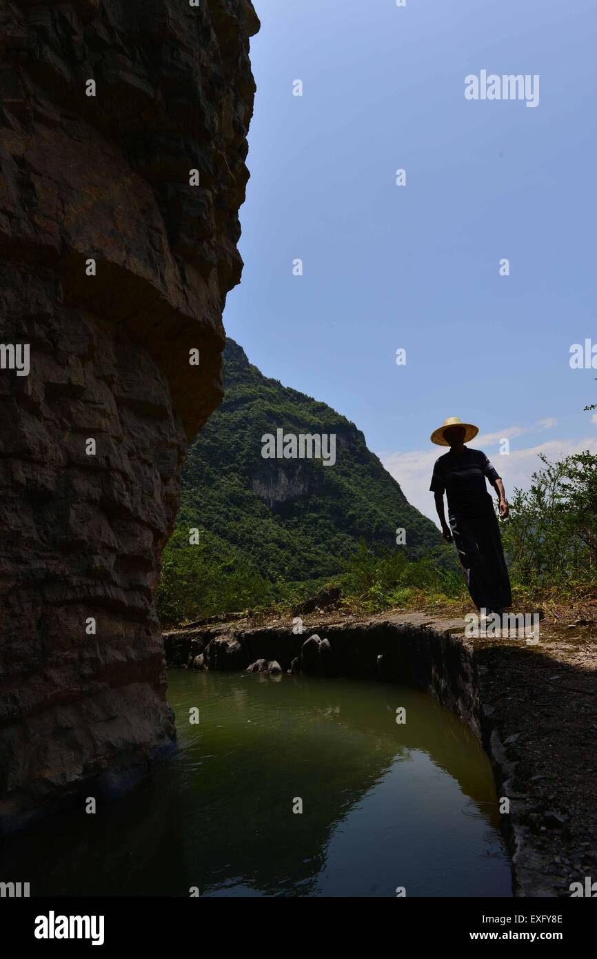 Enshi, Chinas Provinz Hubei. 13. Juli 2015. Dorfbewohner Tan Zushun untersucht den künstlichen Aquädukt Kanal entlang einer Klippe in Badong County von Enshi Tu und Miao-Präfektur, Zentral-China Hubei Provinz, 13. Juli 2015. Künstliches Aquädukt Kanals, Ortung auf einer Höhe von etwa 1.000 Meter mit einer Breite von zwei Metern, Dutzende von Kilometern erstreckt sich entlang einer Klippe von Qingtaiping Stadt Badong County, Changyang County. Das Projekt war begonnene Bau der 1960er Jahre und kostete mehr als 10 Jahren für die Fertigstellung. © Song Wen/Xinhua/Alamy Live-Nachrichten Stockfoto